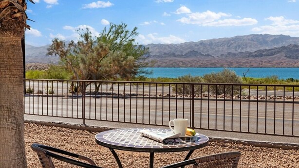 A balcony with a table, a chair, a plant, and a view of a lake and mountains. - Lake Havasu City | Couples Lake Retreat | Pool + Hot Tub (Lake Havasu)