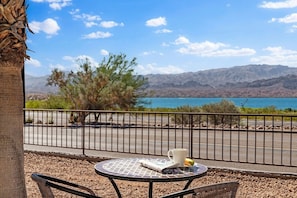 Ein Balkon mit Tisch, Stuhl, Pflanze und Blick auf See und Berge.