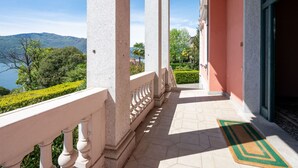 A balcony with a view of a lake and mountains, a tiled floor, and a door with a green and yellow doormat.