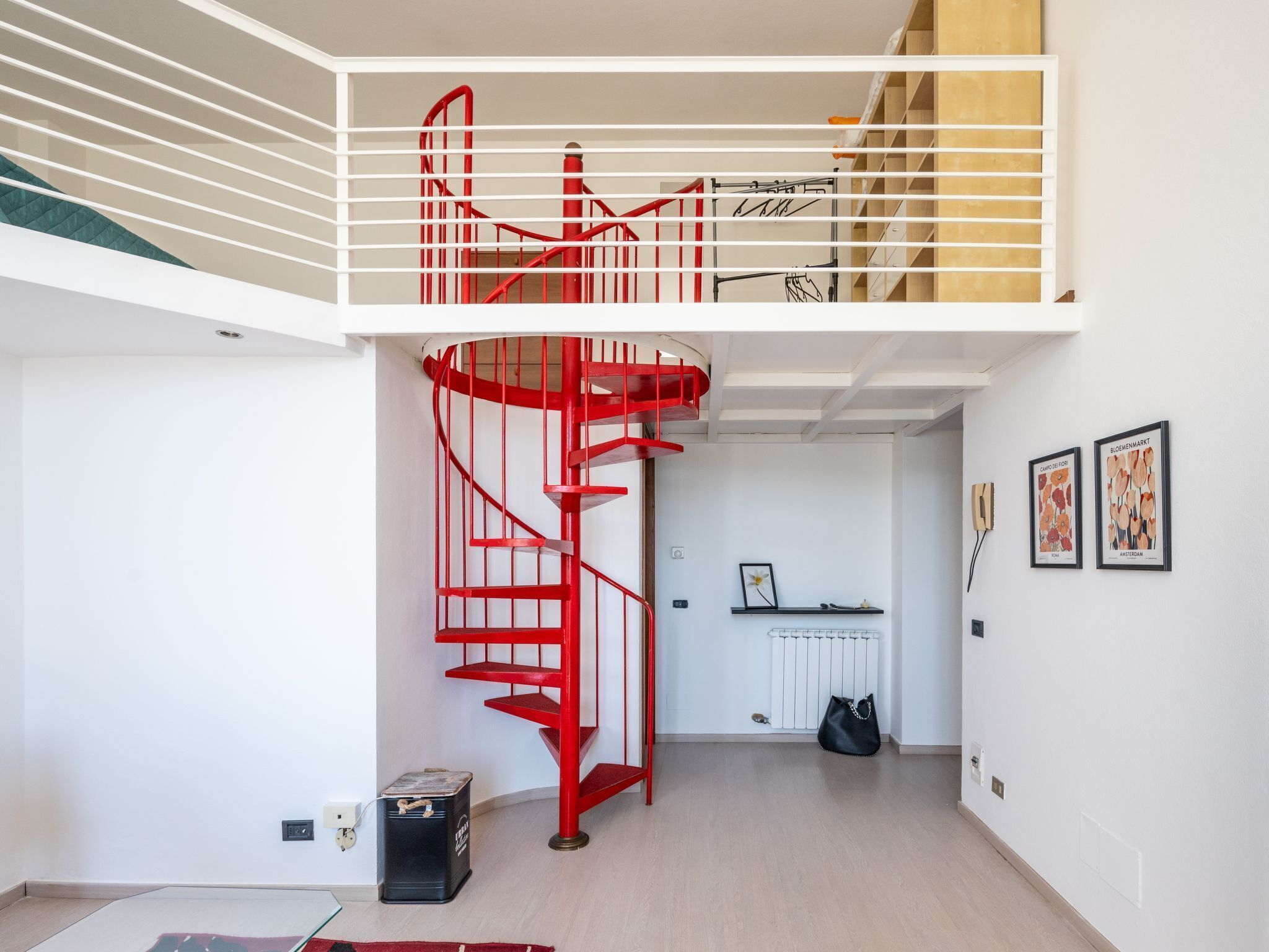 A modern interior with a red spiral staircase, a radiator, and framed botanical prints on the wall.