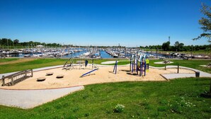 A marina with boats docked, a playground with swings and slides, and a grassy area with a bench. - Cozy ship in Ophoven with lake view (Ophoven)