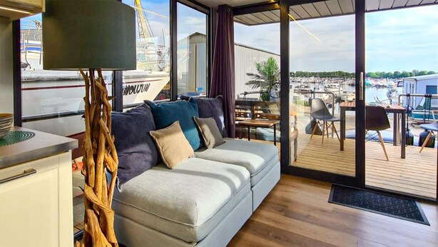 A modern interior with a sofa, a dining area, and a view of a marina. - Cozy ship in Ophoven with lake view (Ophoven)