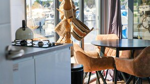 A modern kitchen with a gas stove, hanging woven baskets, and a view of boats through large windows. - Cozy ship in Ophoven with lake view (Ophoven)
