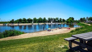 A lakeside park with picnic tables, boats, and people enjoying the area. - Cozy ship in Ophoven with lake view (Ophoven)