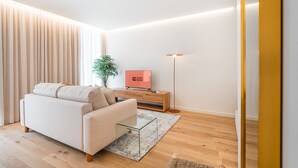 Ein modernes Wohnzimmer mit einer Couch, einem Glastisch, einem Fernseher, einer Stehlampe und einer Pflanze.
