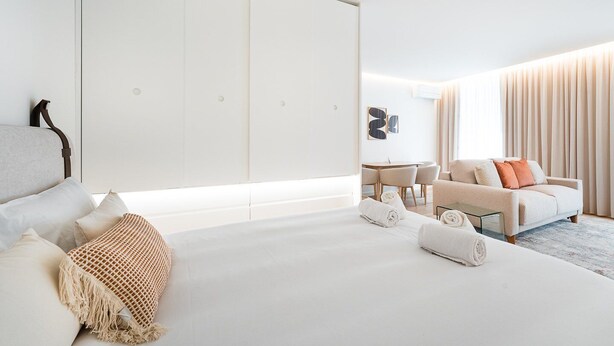 Ein modernes Hotelzimmer mit einem großen Bett, einem Sofa, einem Esstisch und einem Schiebetürenschrank.