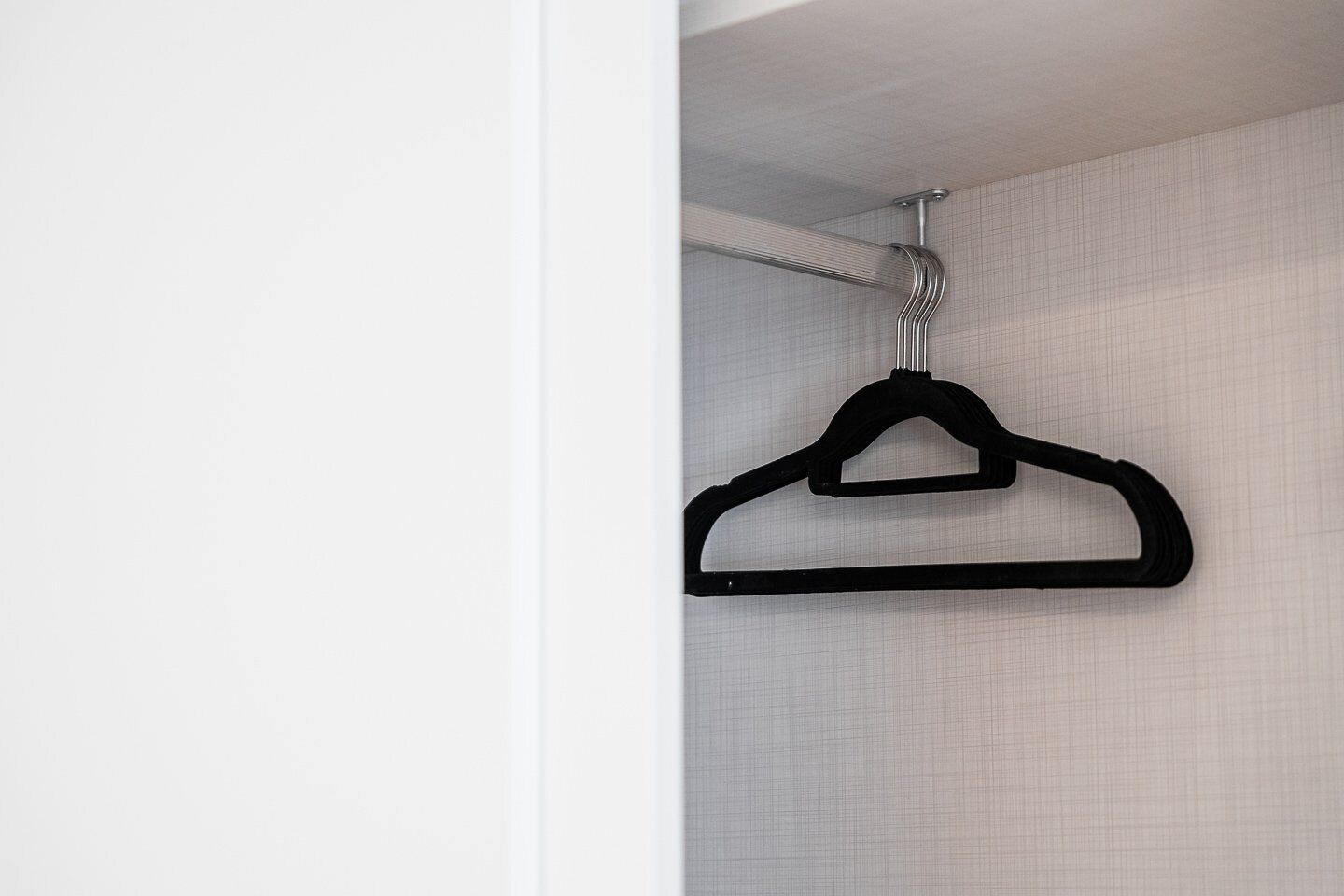 A black hanger hanging from a ceiling hook in a room with white walls and a textured wallpaper pattern.