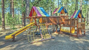 A playground with a slide, climbing net, and a wooden structure with a slide.
