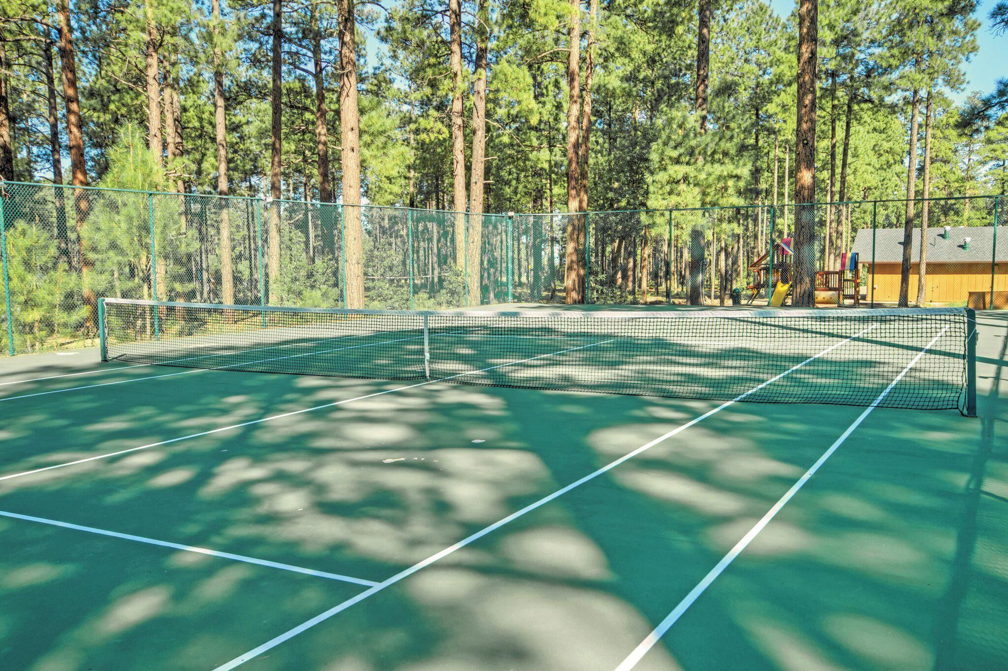 A tennis court surrounded by a metal fence with trees in the background.