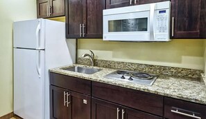 A kitchen with dark wooden cabinets, a white refrigerator, a built-in microwave, a granite countertop, a stainless steel sink, and a gas stove. - Pinetop | Couples Mountain Retreat | Hot Tub + Forest (Pinetop)