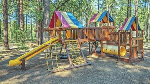 A playground with a slide, climbing net, and a wooden structure with a slide. - Pinetop | Couples Mountain Retreat | Hot Tub + Forest (Pinetop)