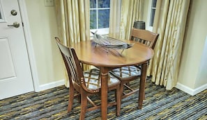 A dining table with chairs, a window with curtains, and a patterned carpet. - Pinetop | Couples Forest Hideaway | Hot Tub + Mountains (Pinetop)