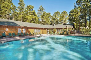 A pool area with lounge chairs, a wooden building, and a forested background.