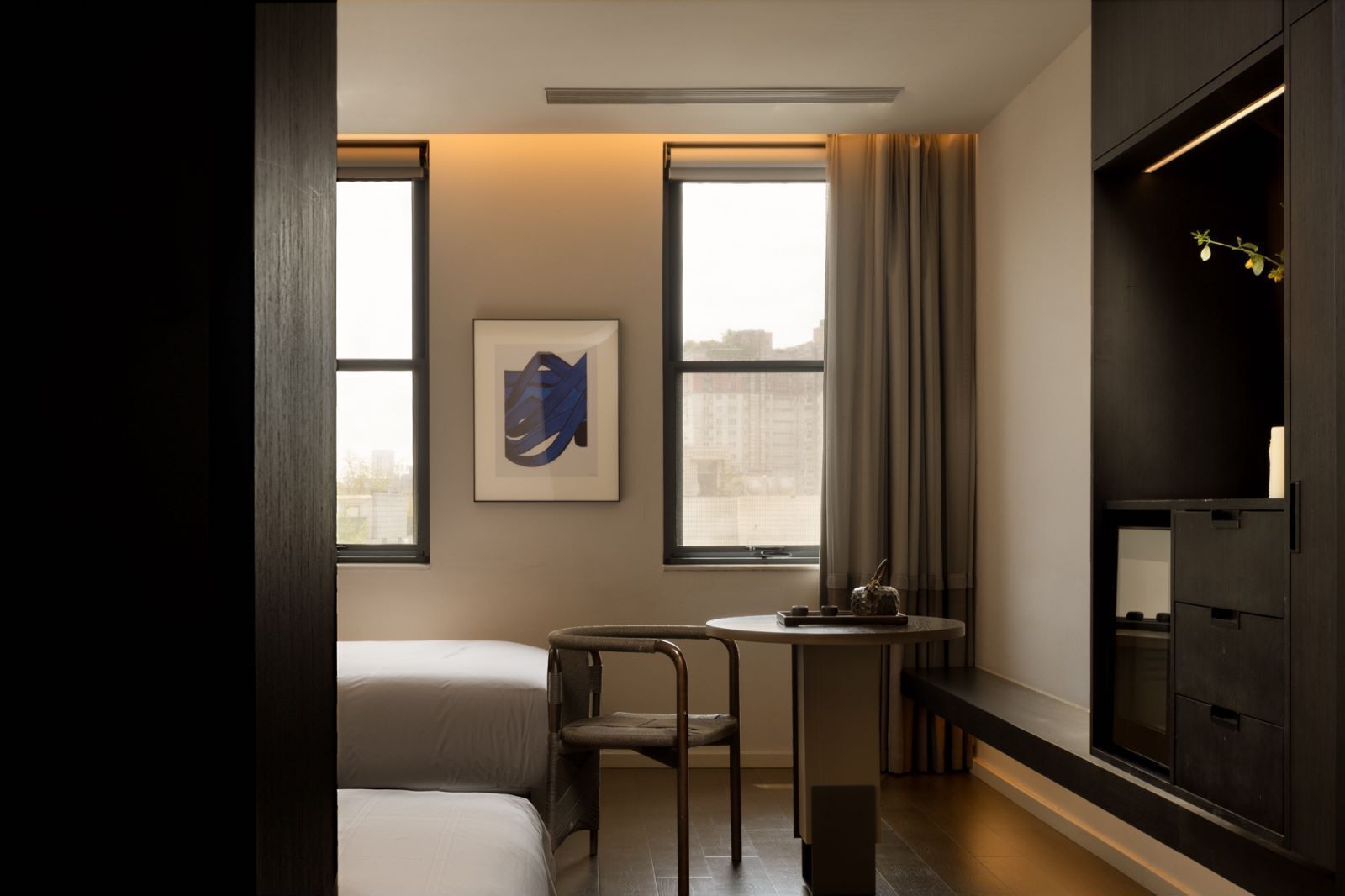 Habitación de hotel pequeña con cama, una mesita, una silla, un escritorio y un ventanal con cortinas.