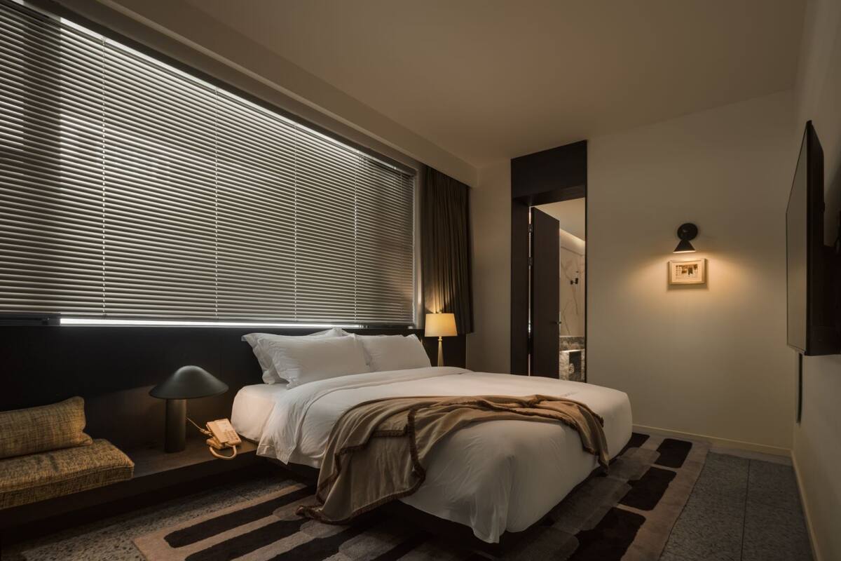 A modern hotel room with a large bed, a bedside table with a lamp, a sofa, and a wall-mounted TV.
