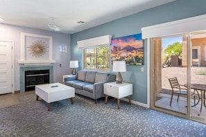 A modern living room with a fireplace, a gray sofa, a coffee table, and a painting of a cityscape. - Oro Valley | Couples Desert Escape | Pool + Hot Tub (Oro Valley)