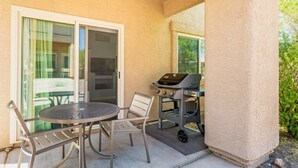 An outdoor patio with a round table and chairs, a grill, and a sliding glass door leading to a covered area. - Oro Valley | Couples Desert Escape | Pool + Hot Tub (Oro Valley)
