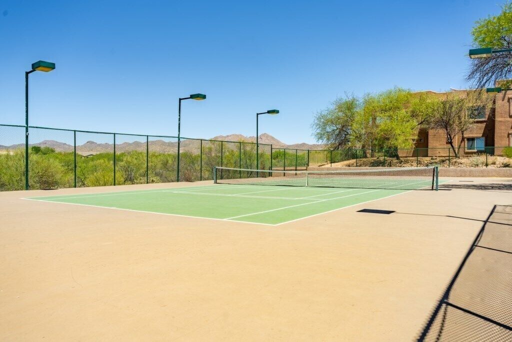 A tennis court with a net, surrounded by a fence and street lamps.