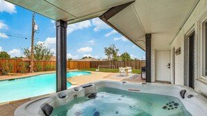A hot tub on a covered deck with a pool in the background. - Stunning Lake House with a Pool and Hot Tub (Lakewood Village)