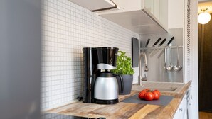 Eine Küche mit einer Kaffeemaschine, einem Topfpflanzen und Tomaten auf der Arbeitsplatte.