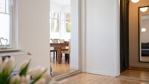 Ein Zimmer mit Holzboden, einem Essbereich mit Tisch und Stühlen sowie einem großen Spiegel an der Wand.