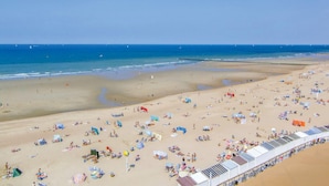 Een strand met veel ligbedden en parasols, een heldere lucht en een rustige zee.