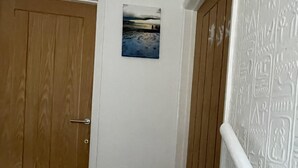 A hallway with a wooden door, a small picture on the wall, and a white textured wall on the right. - 3Bed House, Sleeps 6 near Luton Airport w/ Parking (Luton)