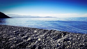 A rocky shoreline with calm water and distant mountains.