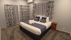 Un dormitorio con una cama grande, dos mesitas de noche, un cabecero y cortinas con estampado floral.