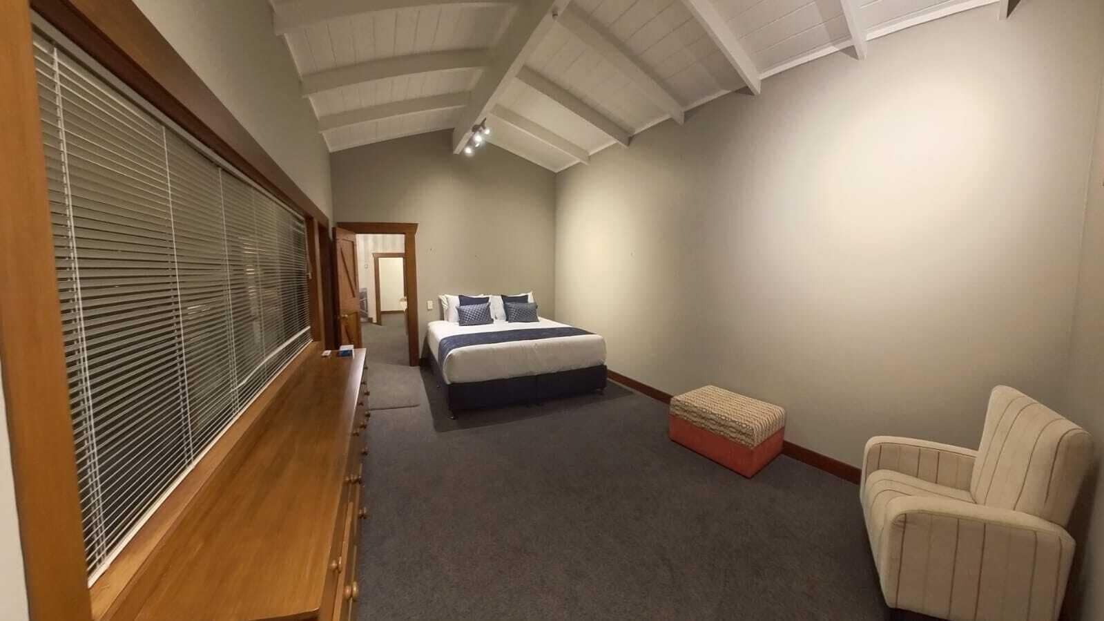 A bedroom with a bed, a chair, a bench, and a window with blinds.