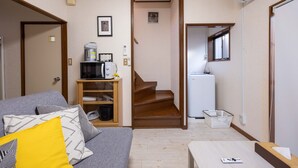 Ein kompakter Wohnraum mit Sofa, Kaffeemaschine, Mikrowelle, Kühlschrank und einer Treppe, die in ein Obergeschoss führt.