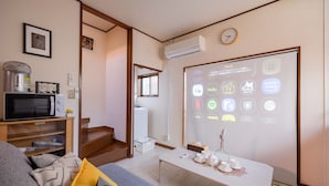 Ein modernes Wohnzimmer mit Flachbildfernseher, Couchtisch mit Dekoration, einer Couch mit Kissen, einer Wendeltreppe und einem an der Wand montierten Projektor, der verschiedene Streaming-Dienste anzeigt.