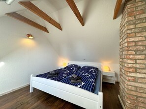 A bedroom with a white bed, wooden beams, a brick wall, and two bedside lamps. - Ferienhaus Leni - Ferienhaus in Gagern (Kluis)