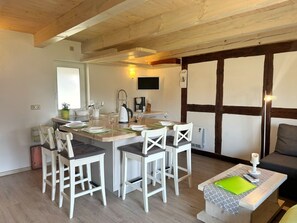 A modern kitchen with wooden beams, a dining area with white chairs, and a cozy seating area with a table and cushions. - Ferienhaus Leni - Ferienhaus in Gagern (Kluis)