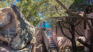 Un escalier en pierre mène à un bâtiment doté d’une porte bleue, qui est entouré d’arbres et de rochers.