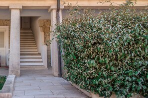 A stone staircase leading to a door, a hedge, and a building facade.