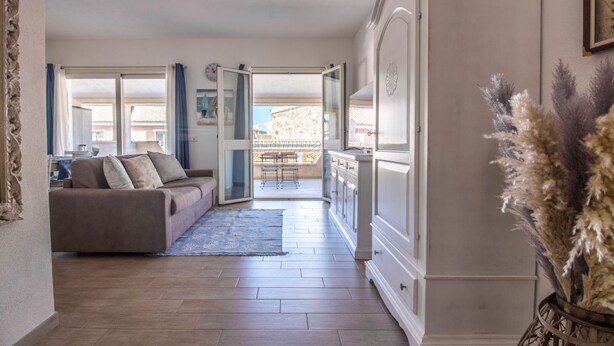 Una sala de estar con un sofá, un comedor con mesa, y vistas a un balcón por una puerta abierta.