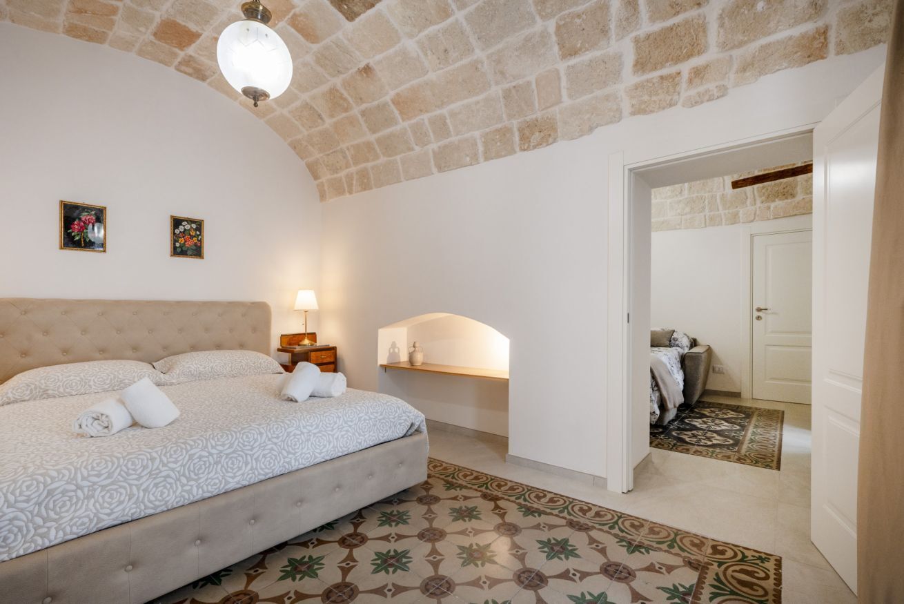 Ein Schlafzimmer mit Bett, Nachttisch, Lampe, einer an der Wand befestigten Ablage und einer Tür zu einem anderen Raum.