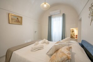 Ein Schlafzimmer mit einem Bett, Handtüchern, einem Gemälde, einer Klimaanlage und einem Nachttisch mit einer Lampe.
