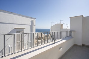 Un balcón con barandilla de metal, un edificio blanco y vista al mar.