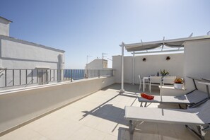 Una terraza en la azotea con zona de estar, una mesa y una planta en maceta.