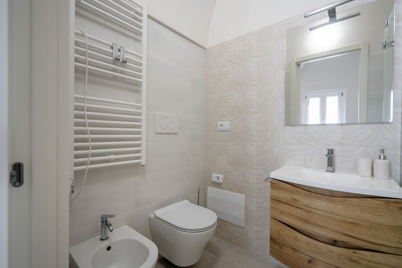 Een badkamer met toilet, bidet, wastafel met spiegel en handdoekhouders.
