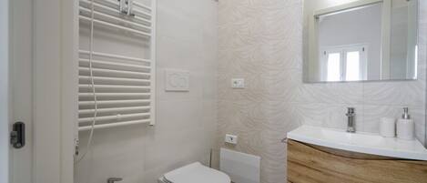 Een badkamer met toilet, bidet, wastafel met spiegel en handdoekhouders.