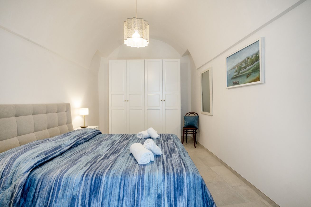 Une chambre à coucher comprenant un lit, une tête de lit, une table de chevet, une chaise, une armoire et un tableau accroché au mur.