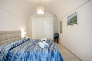 Un dormitorio con cama, cabecera, mesita de noche, una silla, armario y un cuadro en la pared.