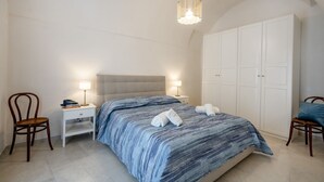 A bedroom with a bed, two bedside tables with lamps, a wardrobe, and two chairs. - GuestHost - Beautiful apartment that accommodates up to 4 people, equipped with all the comforts for a pleasant stay, including a furnished sea-view terrace to enjoy unmissable moments of relaxation. The accommodation is located in a period building with (Monopoli)