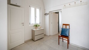 Un pasillo con puertas blancas, un aparador con una planta, una silla azul y un estante con ganchos.