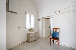 A hallway with white doors, a dresser with a plant, a blue chair, and a wall-mounted shelf with hooks.