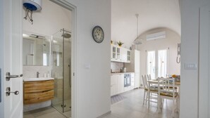 Una cocina moderna con armarios blancos, una zona de comedor con mesa y sillas, y un box de ducha de vidrio.