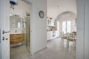 Una cocina moderna con armarios blancos, una zona de comedor con mesa y sillas, y un box de ducha de vidrio.